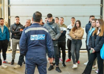 A technical superintendent wearing a blue uniform with INJEGOV's logo stand in front of a group of marine technical high school students
