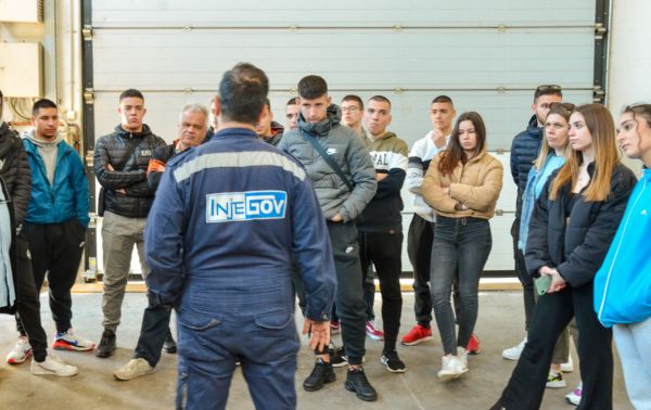 A technical superintendent wearing a blue uniform with INJEGOV's logo stand in front of a group of marine technical high school students