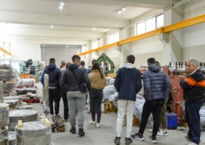 A group of students is guided inside a large building with many engine spare parts